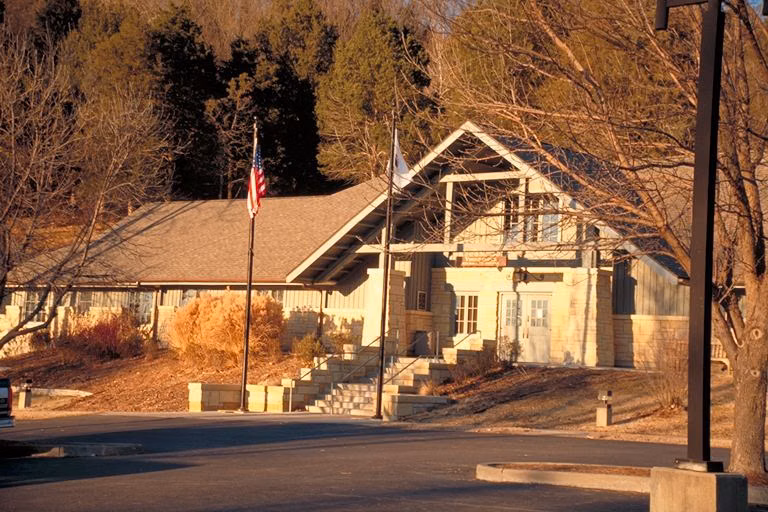 A rustic stone and timber CCC-era lodge building with a flag out front in low evening sun